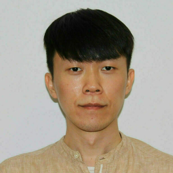 Young man with short black hair and a neutral expression looks forward. He wears a tan collared shirt over a white undershirt.